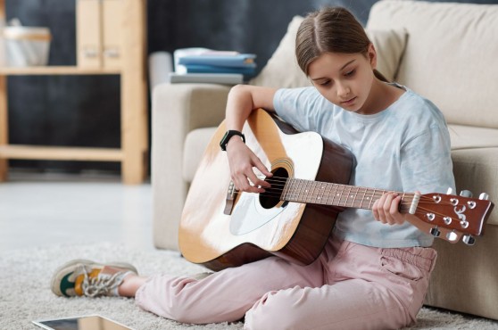 Niña tocando la guitarra en su habitación.